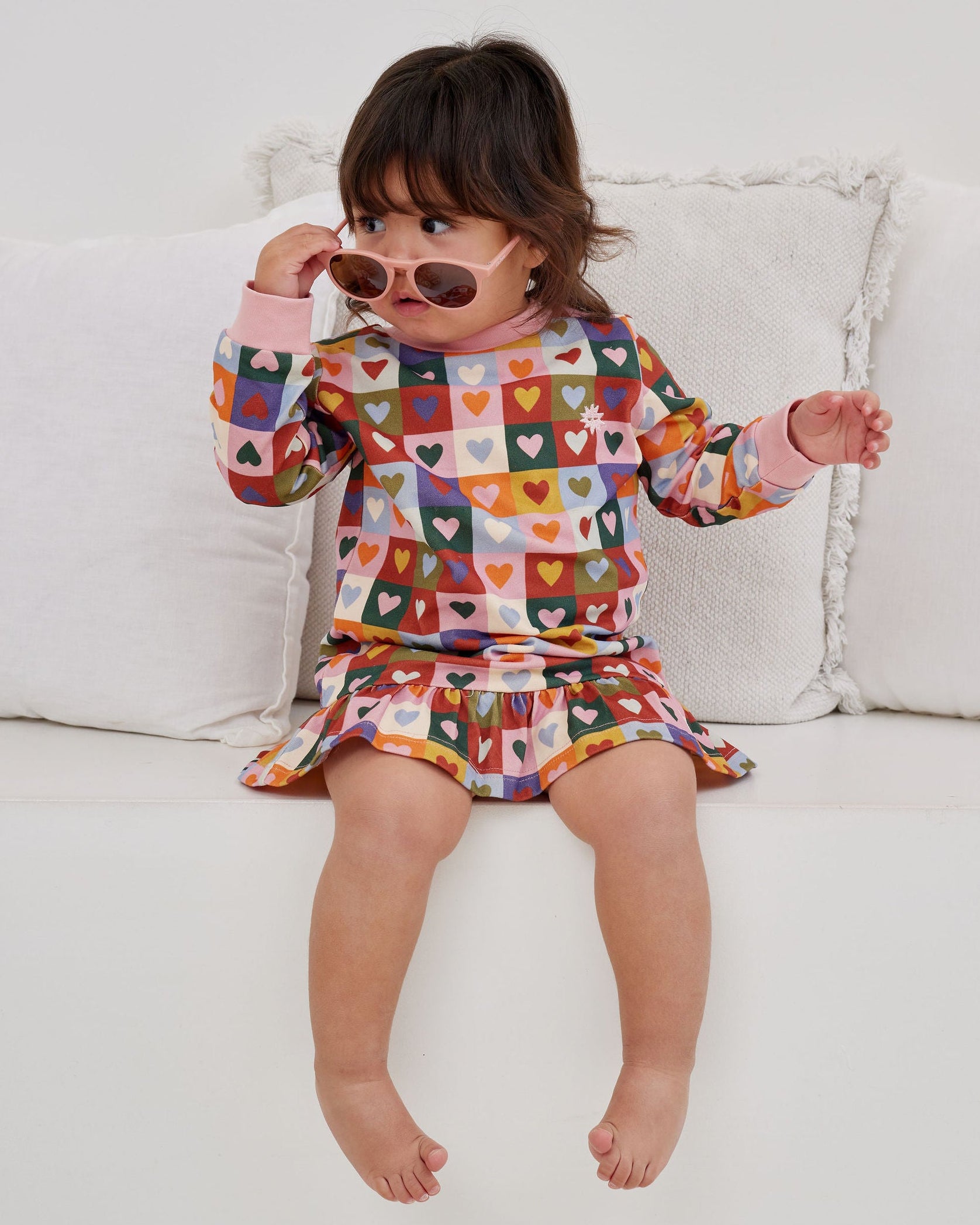 Child wearing a colorful patterned outfit sitting on a white couch.